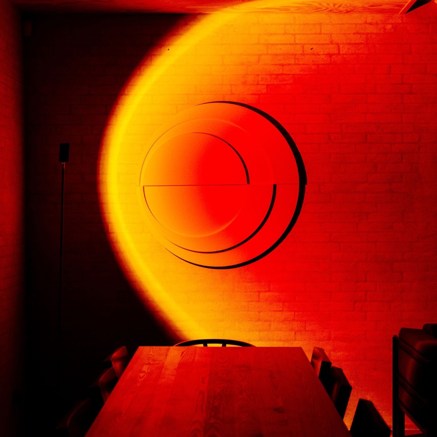 Rundt 3D vægpanel oplyst af rød og gul lyskunst skaber dramatisk dybde og akustisk effekt i et stemningsfuldt rum.