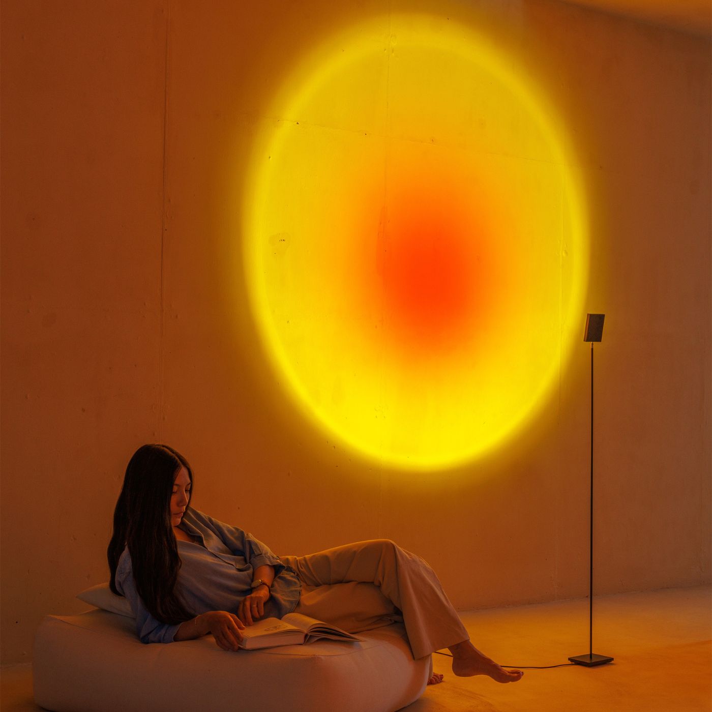 Blødt oplyst rum med cirkulært lys og 3D vægpaneler der skaber en beroligende stemning omkring en læsende kvinde.