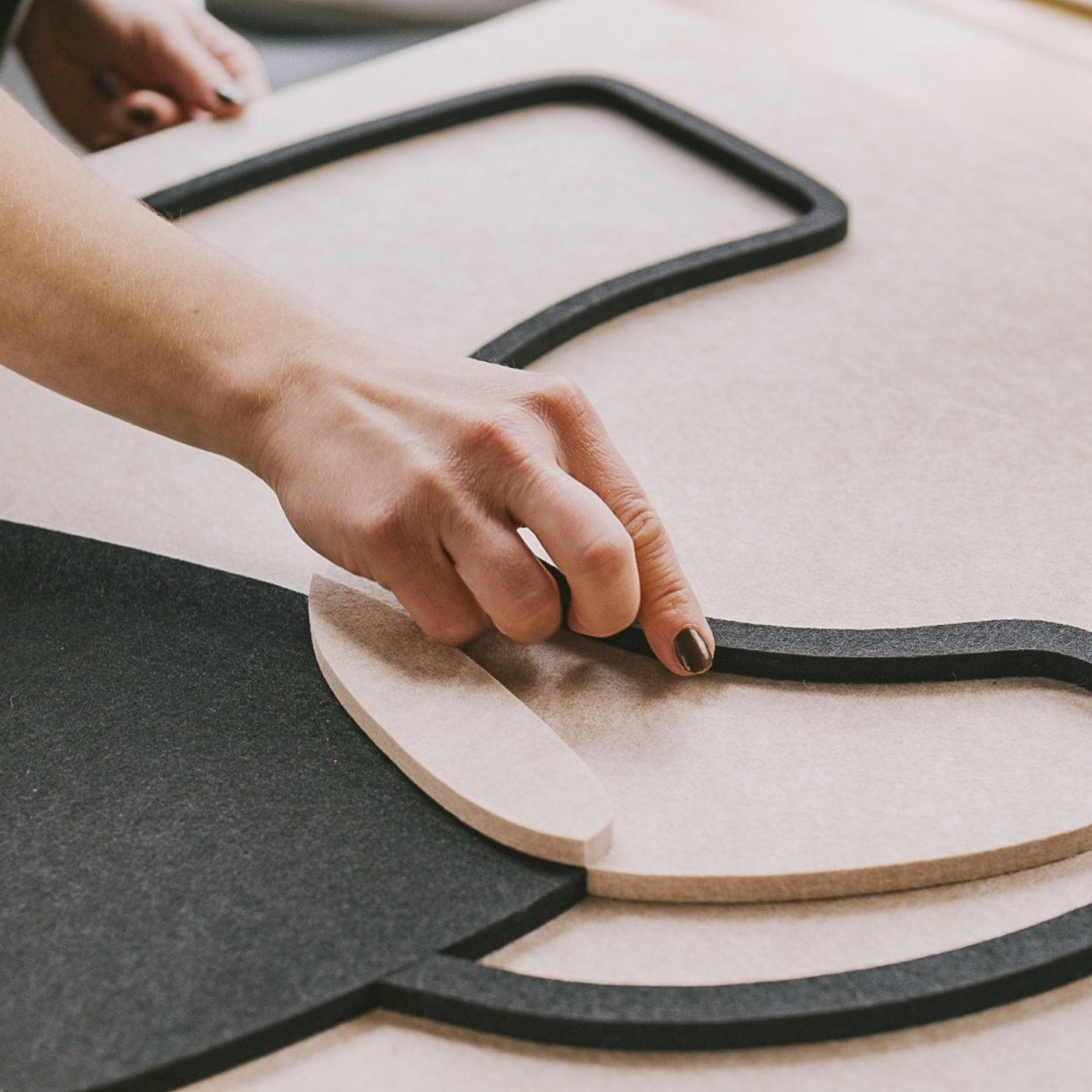 Detalje af hånd, der arbejder med former og materialer i skabelsen af vægpanel inspireret af minimalistisk kunst.