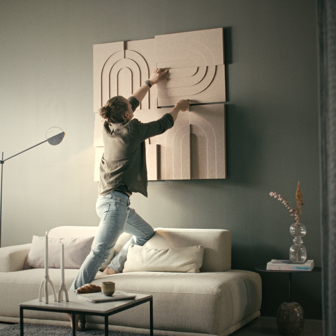 Mand justerer akustiske kunstpaneler på en stuevæg, der forbedrer akustikken i et rum med moderne lydabsorberende design.
