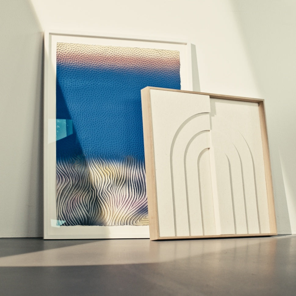 Arturel X Kvadrat akustikpanel i beige ved siden af et farverigt kunstværk, begge med egetræsramme