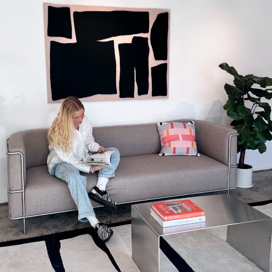 Kvinde læser i sofa under stort akustikbillede i Nordic Bauhaus design i moderne og roligt stuemiljø.